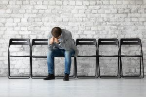 A sad jobless man puts head on two closed hands while sitting on a chair