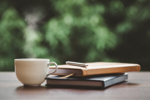 Hot coffee, books, and a pen on a table with green trees as a background