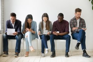 People sitting in line looking at their own paper and looking in their phone