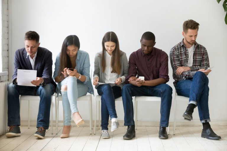 People sitting in line looking at their own paper and looking in their phone