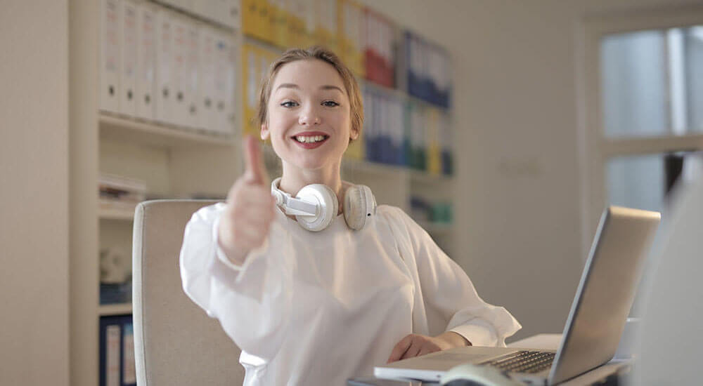 Woman Wearing White Top While Doing Thumbs Up in front of a laptop - Spartanburg County - Careers In Government