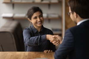 An employee welcoming an Indian woman to a successful job with a handshake