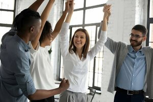 A group of People celebrating at the office with hands raised on air