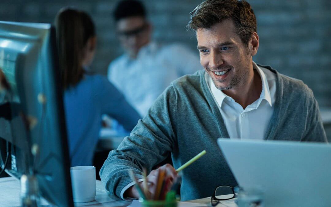 A man smiling in front of a desktop inside a dim office