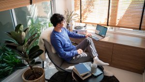 A young Asian man relaxing while navigating his laptop