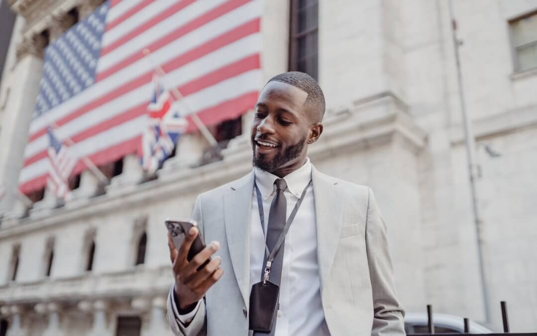 An African American man, in front of a building with a flag.