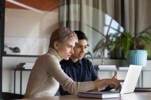 A corporate teacher showing new employee a learning video on laptop