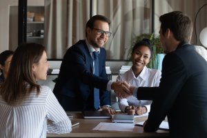 A man welcoming a guy to the team while his colleagues smiles at him