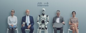 Four people and a humanoid robot sit in chairs against a wall. A sign that reads "Government Job Interview" with an arrow pointing right is above them. One person holds a tablet, another a coffee cup, one is using a laptop, and the last sits with hands on their lap.
