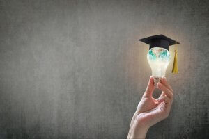 A hand holding a bulb with a graduation cap