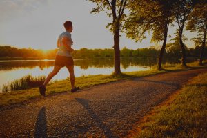 A young man jogging in a park during sunset beside a lake
