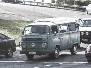 A vintage blue Volkswagen van with a "002-LAB" plate drives along a road in the City of Albany, surrounded by cars. The van appears weathered, showing visible signs of age and character.