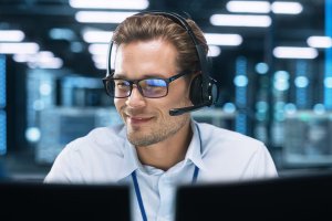 A staff with headphones talking to clients while facing his desktop