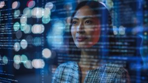 A woman is looking at a screen displaying lines of code, with city lights blurred in the background. The image conveys a sense of AI and data analysis. The woman appears thoughtful and focused.