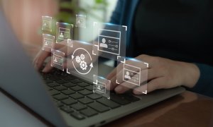 A person types on a laptop with floating digital icons representing AI, data, and settings surrounding their hands. The background is slightly blurred, highlighting the technology interface elements in the foreground.