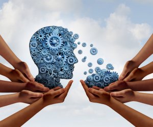 A human head made of interlocking blue gears is supported by multiple hands. Small gears appear to be falling from the head into the hands below, all against a cloudy sky background. The image symbolizes cooperation and collaboration in sharing knowledge, much like an effective government working together.