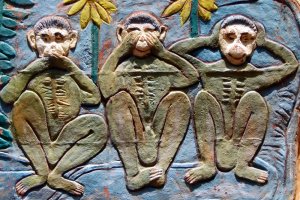 A colorful relief sculpture depicts the Three Wise Monkeys: one covering his mouth, the next covering his eyes, and the last covering his ears. Painted in green and surrounded by leaves and flowers on a textured background, this piece serves as a whimsical reminder for any workplace.