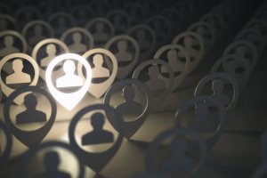 An array of person icons within location pins are depicted in a darkened background, representing the workforce. One icon is prominently illuminated, highlighting it among the others. The other icons recede into the dark background, creating a sense of depth and focus on the highlighted figure.