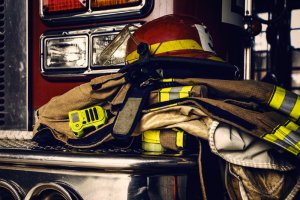 Firefighter gear, including a helmet, protective jacket, and radio, is neatly placed on the metal step of a fire truck equipped with AI. The red truck features reflective lights and a shiny surface, suggesting readiness for an enhanced emergency response.