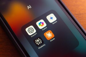 A smartphone screen displays a folder labeled “AI” containing five app icons—ChatGPT, Copilot, Gemini, Perplexity, and Claude—highlighting essential tools increasingly integrated into modern workforces against a blurred background.
