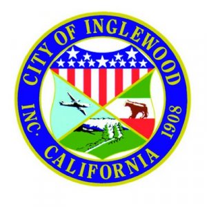 Seal of the City of Inglewood, California, featuring a shield with stars, stripes, a plane, mountains, trees, and a horse, surrounded by a blue and yellow circular border with text.