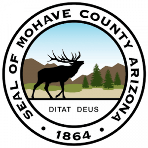 Seal of Mohave County, Arizona, featuring a silhouette of an elk, trees, mountains, and sky, with the motto “DITAT DEUS” and the year 1864. Text encircles the seal’s border.
