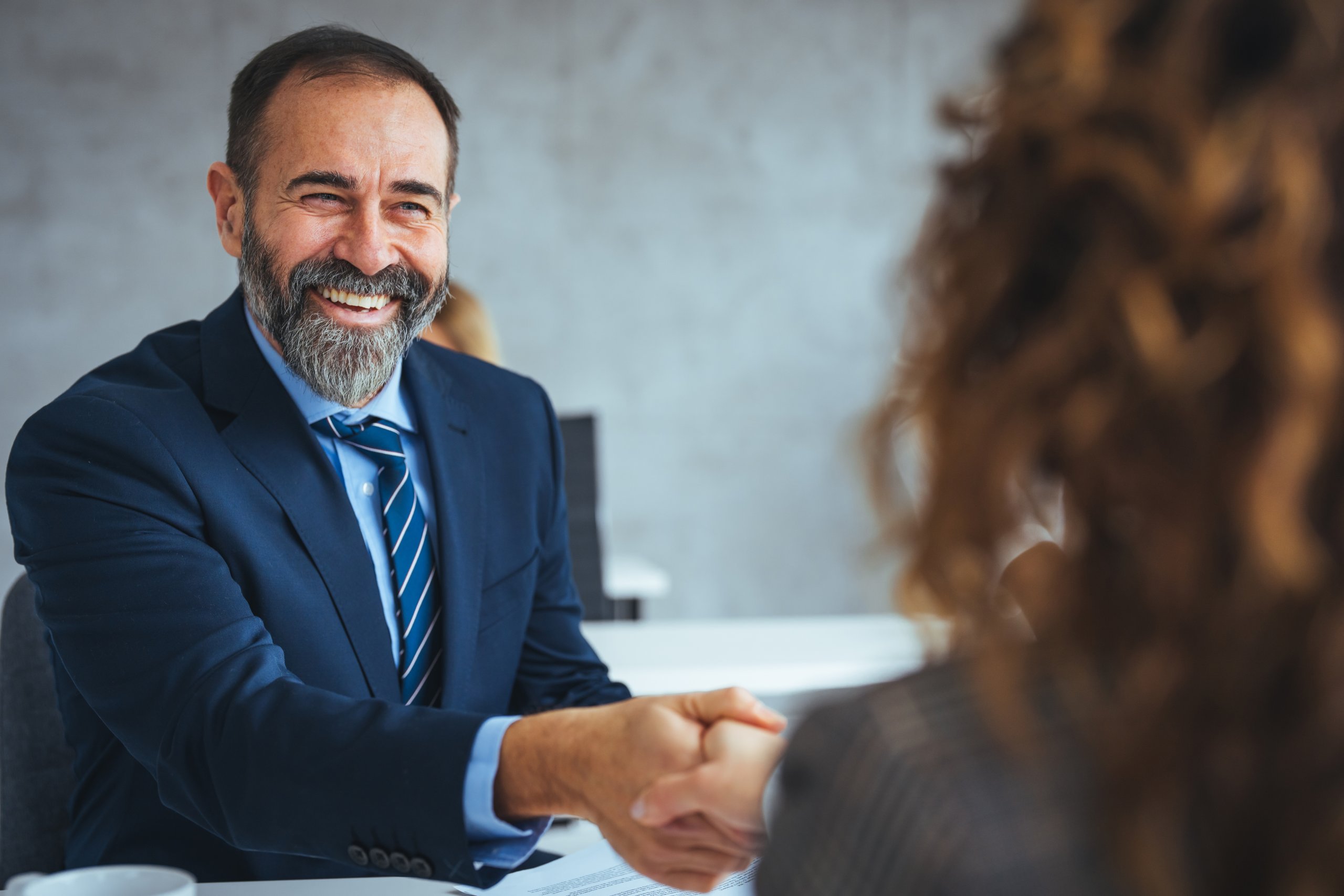 Happy,Senior,Entrepreneur,Came,To,An,Agreement,With,His,Colleague Four people in business attire sit in a row, using laptops, tablets, and smartphones—highlighting a professional, tech-savvy environment where AI seamlessly integrates into daily workflows. Only their lower bodies are visible.