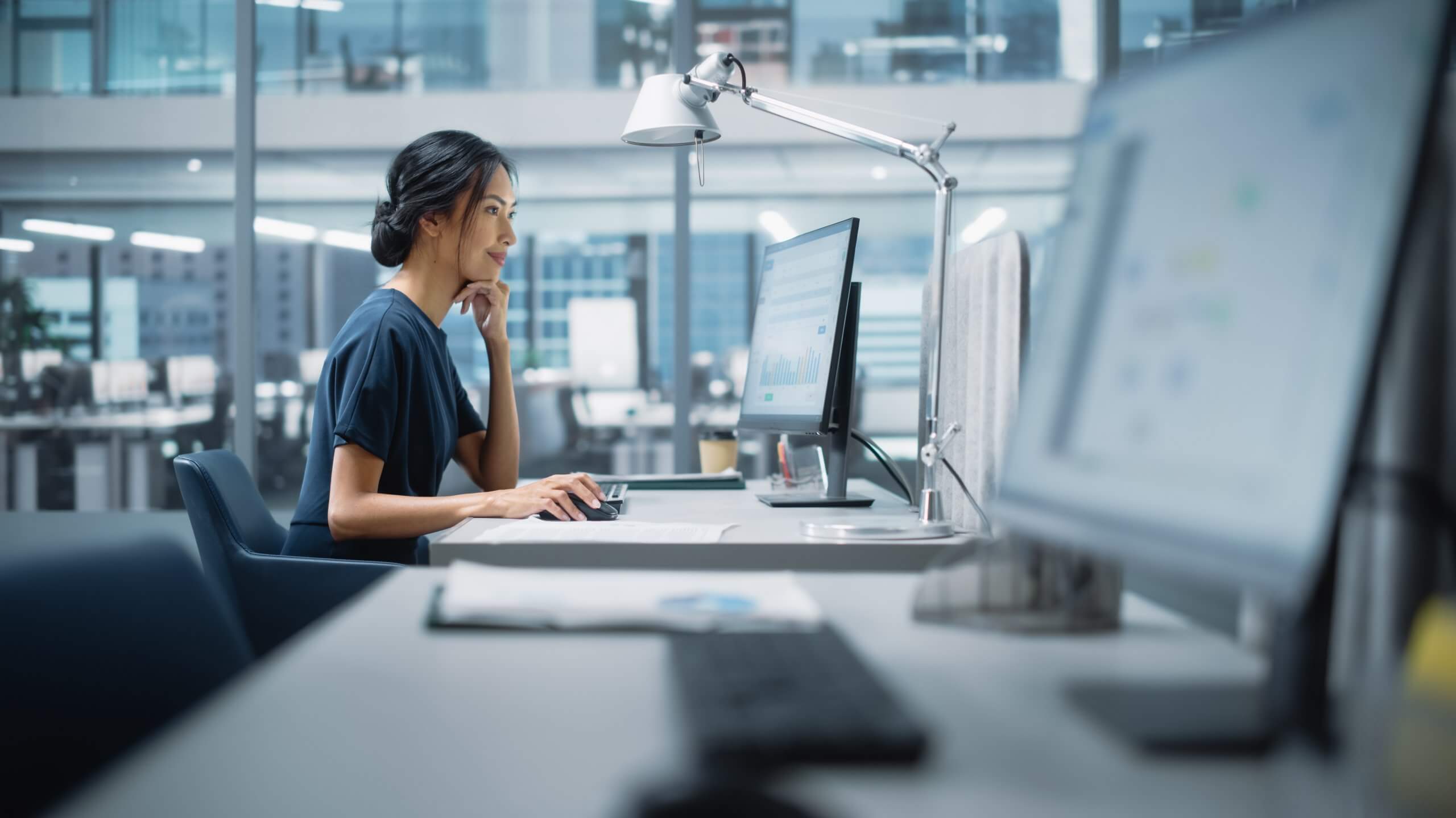 A woman sits at a desk in a modern office, focused on her computer. Her hand rests on her chin as she analyzes data to boost performance. The bright workspace features large windows and other desks in the background. A woman sits at a desk in a modern office, focused on her computer. Her hand rests on her chin as she analyzes data to boost performance. The bright workspace features large windows and other desks in the background.