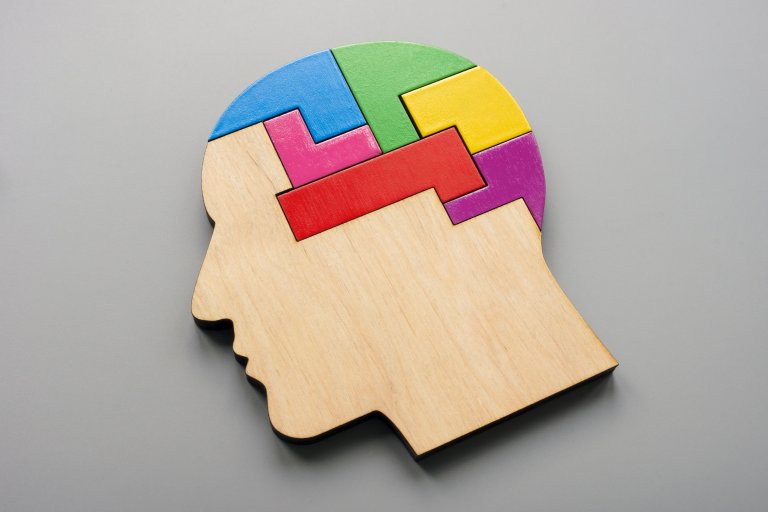 A wooden puzzle in the shape of a human head is filled with colorful, interlocking pieces on a gray background, symbolizing different aspects of an employee’s mind and creative problem-solving.