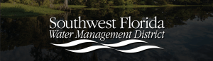 Logo for Southwest Florida Water Management District, featuring white text and wave graphics over a calm water body, with green trees and vegetation from the Water Management District reflected on the surface.