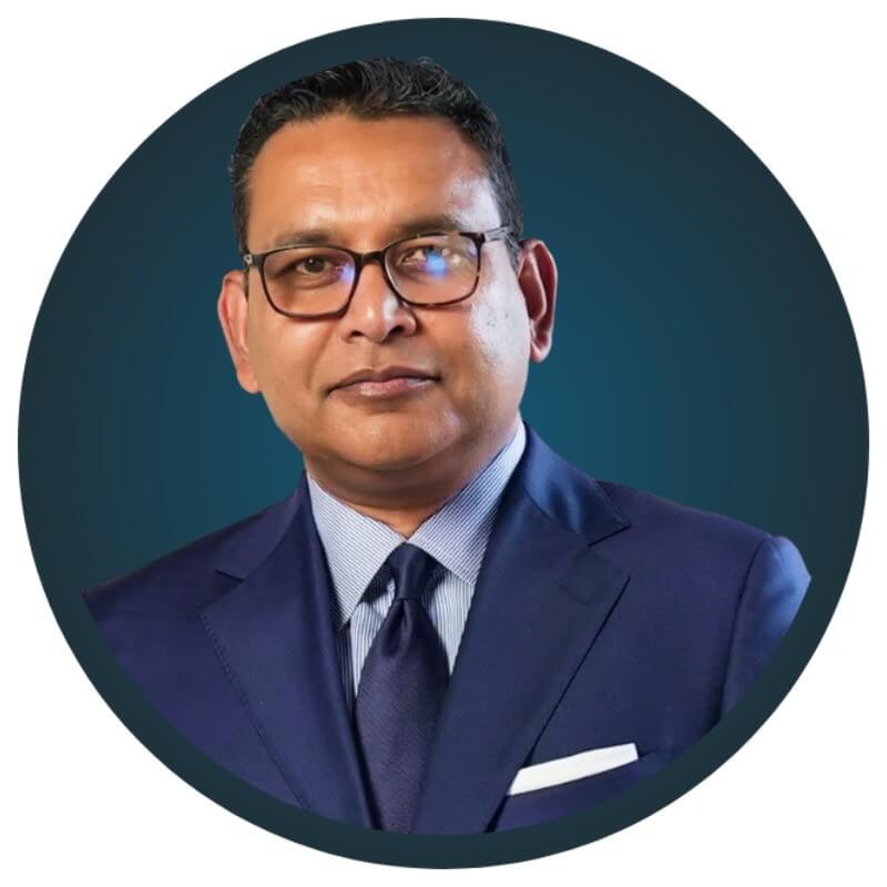 A man wearing glasses and a navy blue suit with a tie and pocket square poses for a professional headshot against a dark teal circular background.