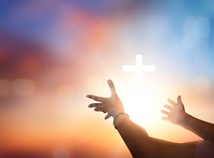 Outstretched hands reaching toward a glowing white cross with a colorful sky in the background, symbolizing faith, hope, spirituality, and the pursuit of success.