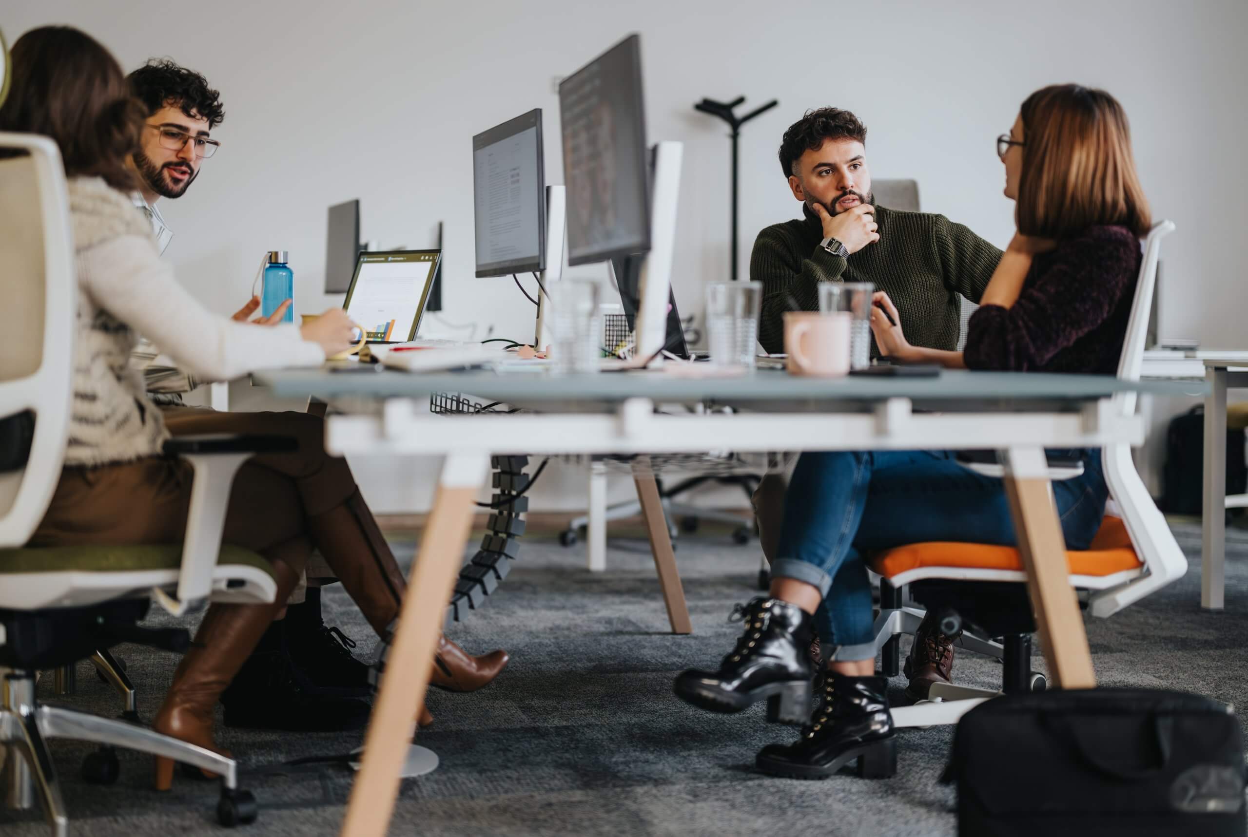 A man and a woman sit across from each other at an office desk, smiling and engaged in conversation as they learn from one another. The desk holds a tablet, papers, and a glass of water, set against a bright, modern office space.