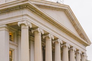 The image shows the neoclassical facade of a federal government building with large columns and the words "The Treasury Department" engraved above them.