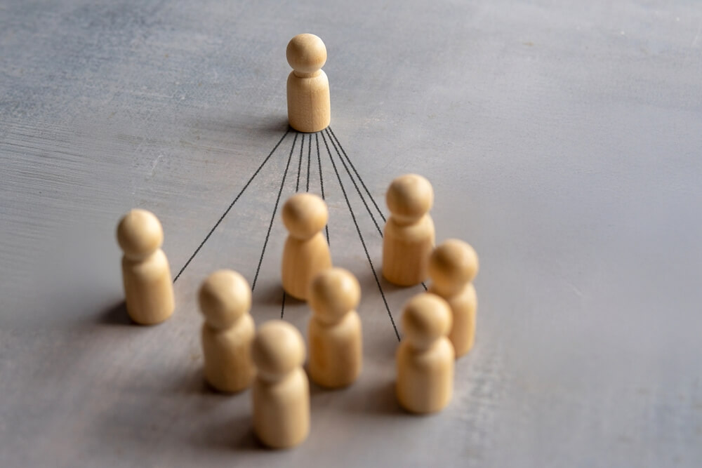 Nine wooden figurines in a group are connected by black lines to a single wooden figurine standing in front, representing leadership or influence within a group—a visual metaphor for public service and guiding others. Nine wooden figurines in a group are connected by black lines to a single wooden figurine standing in front, representing leadership or influence within a group—a visual metaphor for public service and guiding others.