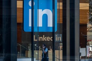 A person talks on the phone while walking past the entrance of a building with large LinkedIn logos, perhaps discussing new opportunities in the Public Sector.
