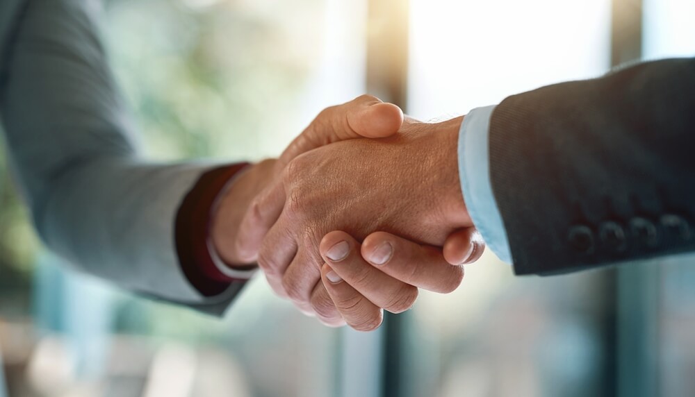 Two workers in business suits shaking hands, symbolizing agreement or partnership, with a blurred office background. Two workers in business suits shaking hands, symbolizing agreement or partnership, with a blurred office background.