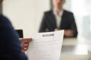 A person holds a resume during a government job interview, with another person in a suit sitting across the desk, slightly out of focus.