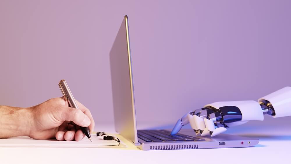 A human hand writes on paper while a robot hand types on a laptop keyboard, separated by the screen, symbolizing collaboration between government workers and artificial intelligence. A human hand writes on paper while a robot hand types on a laptop keyboard, separated by the screen, symbolizing collaboration between government workers and artificial intelligence.
