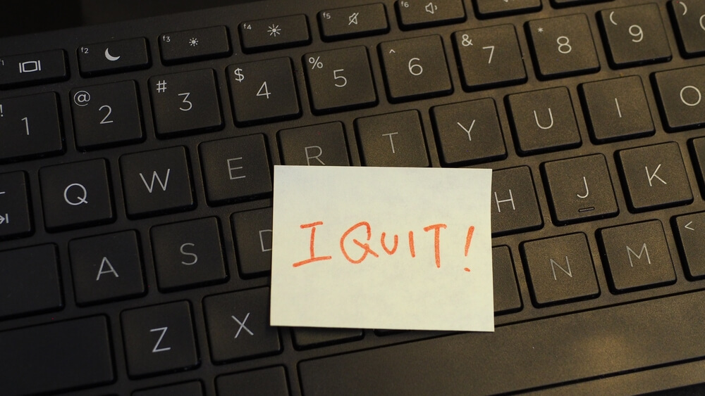 Side,View,Of,Yellow,Adhesive,Note,With,Handwritten,Capital-letter,Words A woman wearing glasses and a zebra-print sweater works on a tablet at a long wooden table in a modern, brightly lit office space that reflects a vibrant and collaborative culture. Colorful sticky notes are on the table near her hand.