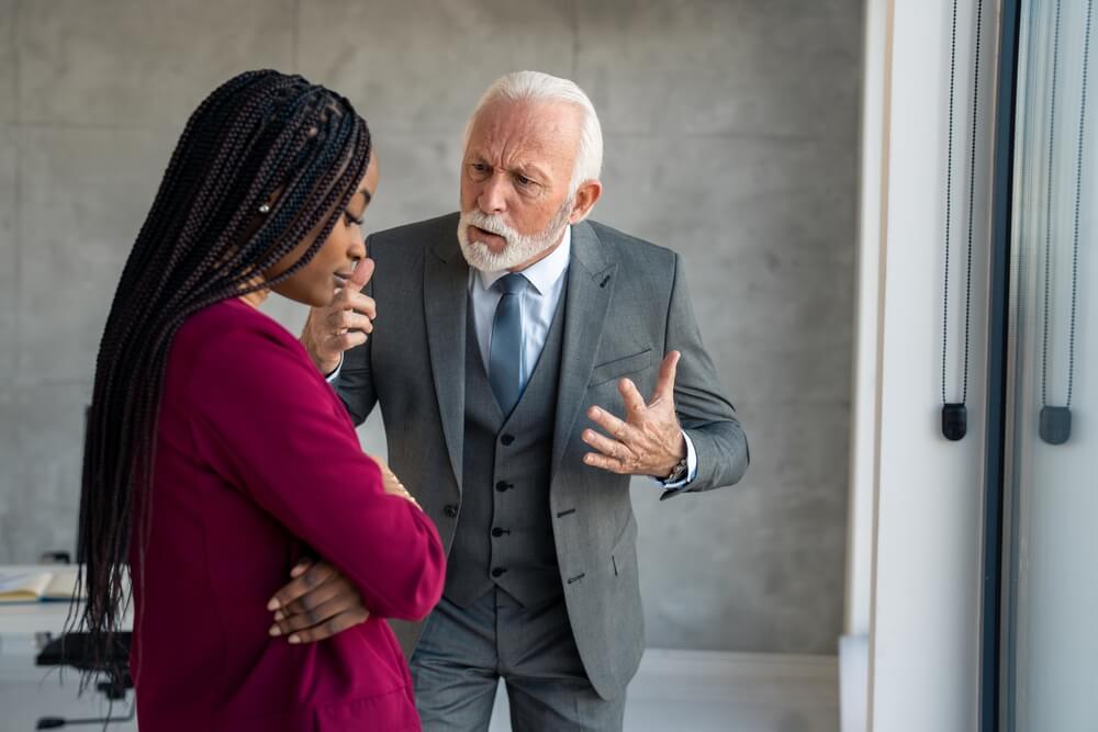Furious,Senior,Businessman,Company,Manager,Yelling,At,Young,Businesswoman,Putting Three coworkers stand in an office hallway, embodying a positive workplace culture; two men are giving each other a high-five while a woman next to them smiles and holds a notepad.